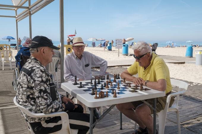  Tres personas juegan al ajedrez a la sombra en la playa de Levante de Benidorm.