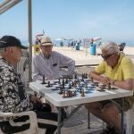  Tres personas juegan al ajedrez a la sombra en la playa de Levante de Benidorm.