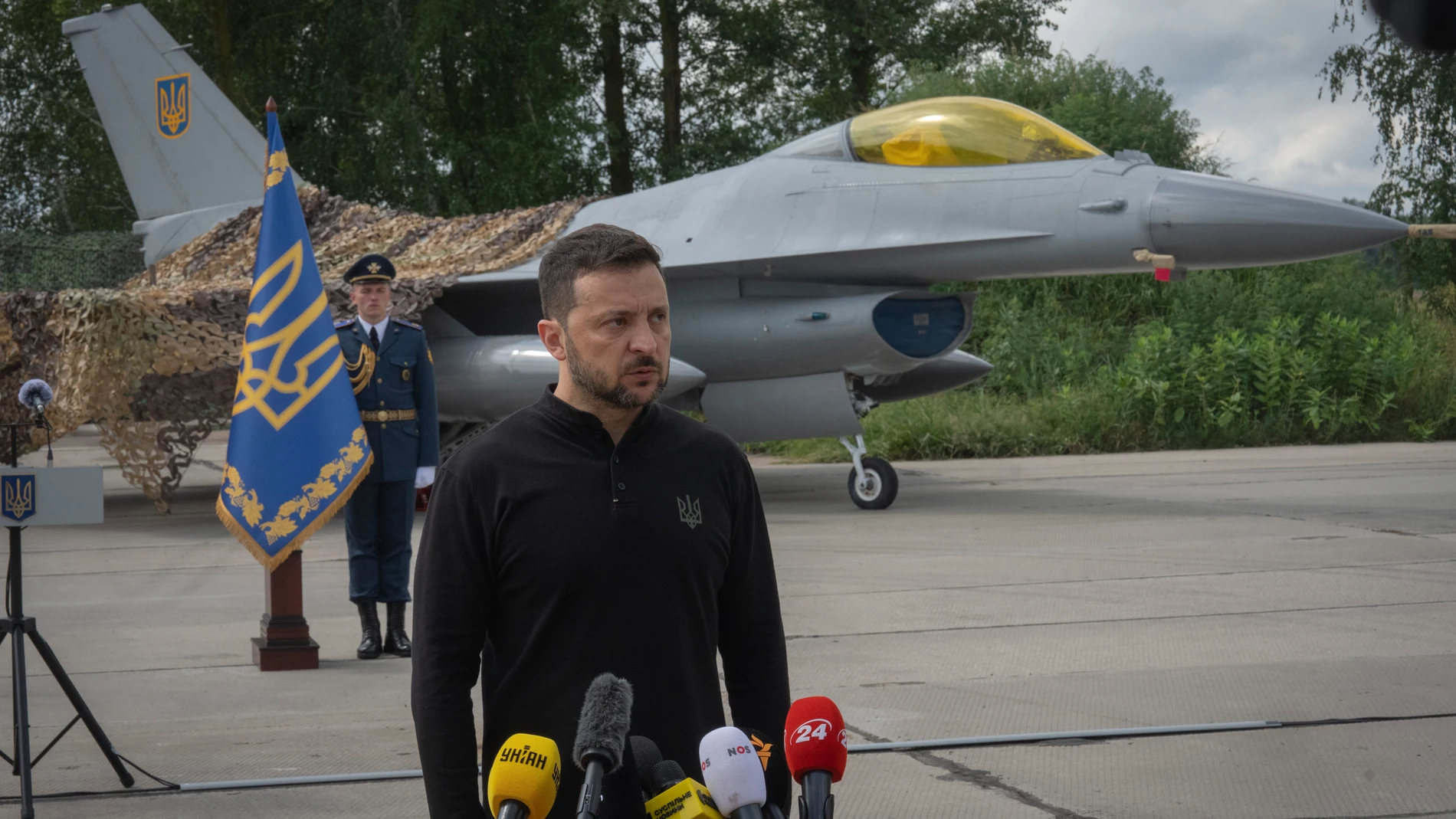 Ukraine's President Volodymyr Zelenskyy answers media questions standing against the background of Ukraine's Air Force's F-16 fighter jets in an undisclosed location in Ukraine, Sunday, Aug. 4, 2024. (AP Photo/Efrem Lukatsky)