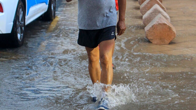 Una persona vadea una calzada anegada por la lluvia