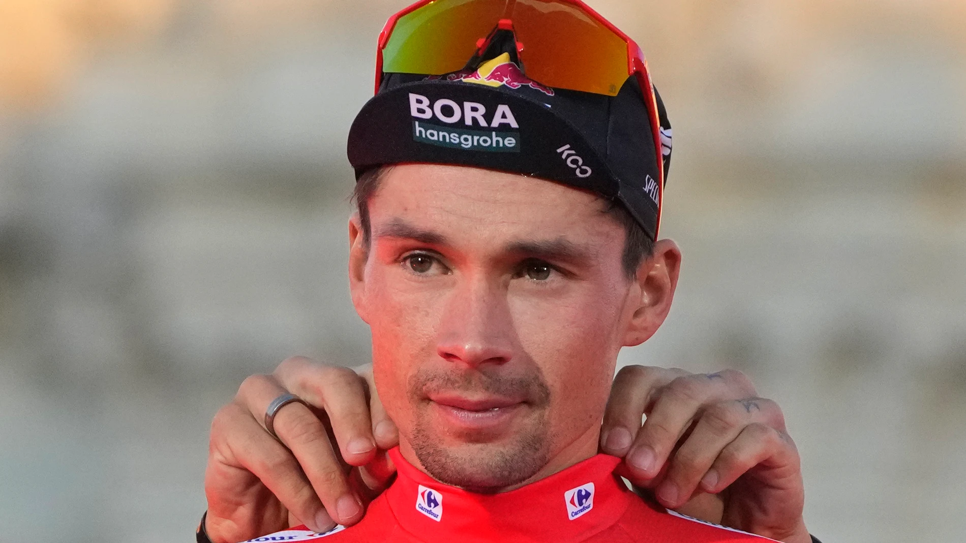 Primoz Roglic of Slovenia gets help putting on his red jersey after winning La Vuelta cycling race during the last stage in Madrid, Spain, Sunday, Sept. 8, 2024. (AP Photo/Paul White)