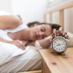 Mujer durmiendo con una mano en el despertador