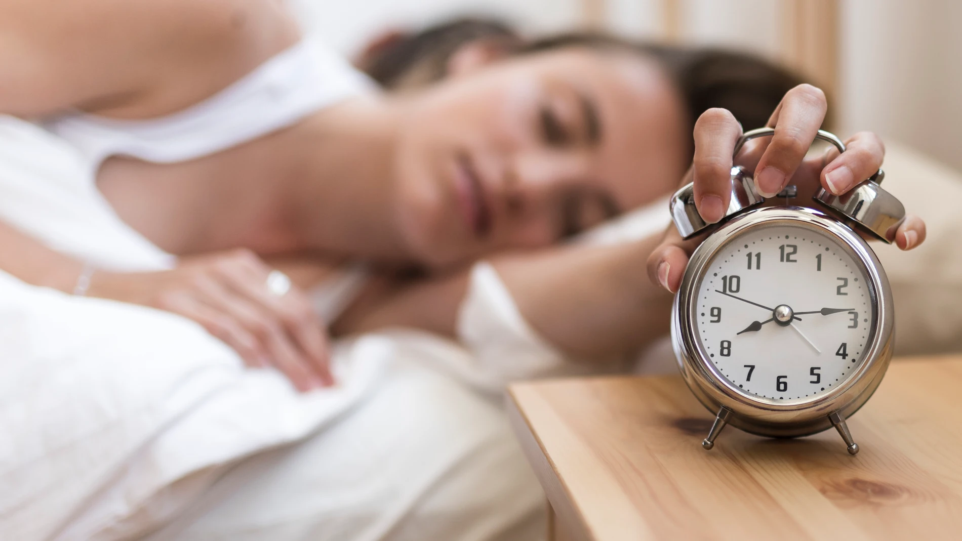 Mujer durmiendo con una mano en el despertador