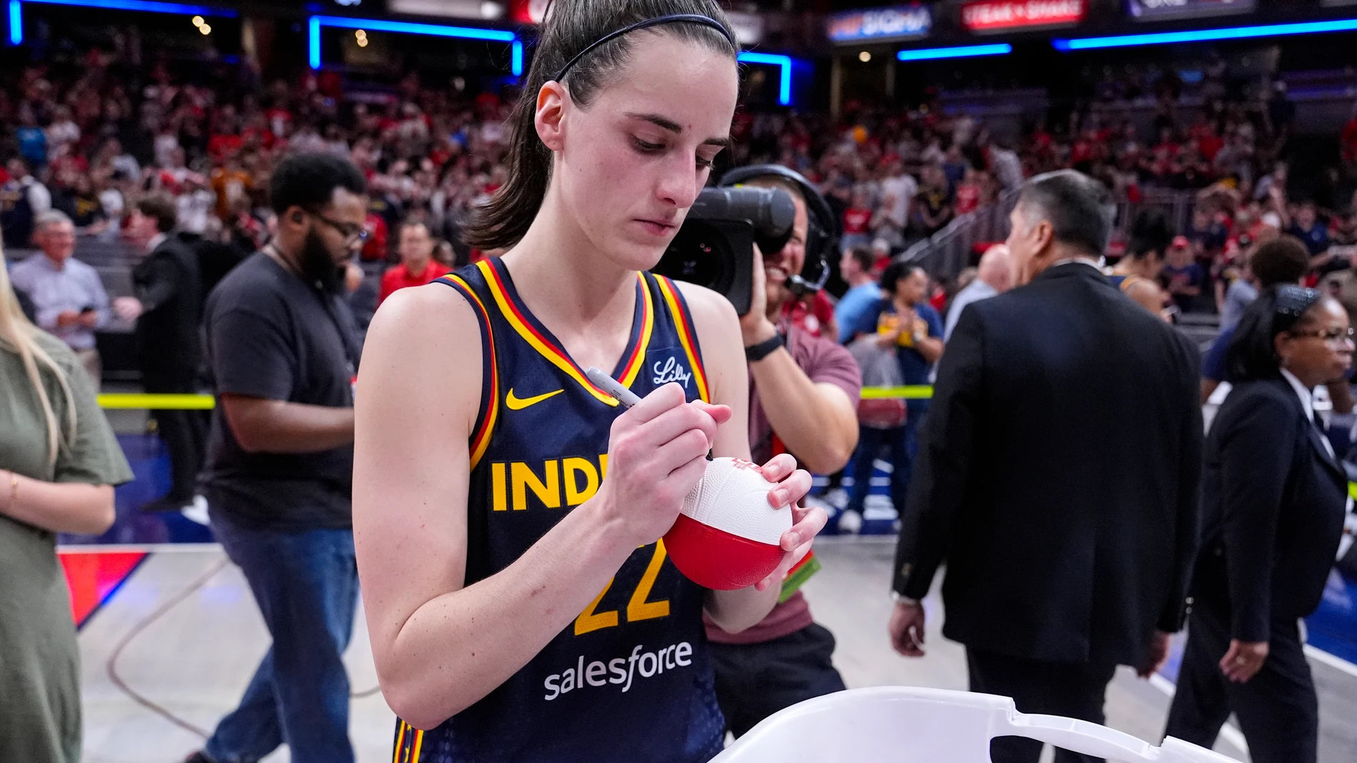 Indiana Fever guard Caitlin Clark (22) signs mini basketballs for fans following in a WNBA basketball game against the Dallas Wings in Indianapolis, Sunday, Sept. 15, 2024. (AP Photo/Michael Conroy)