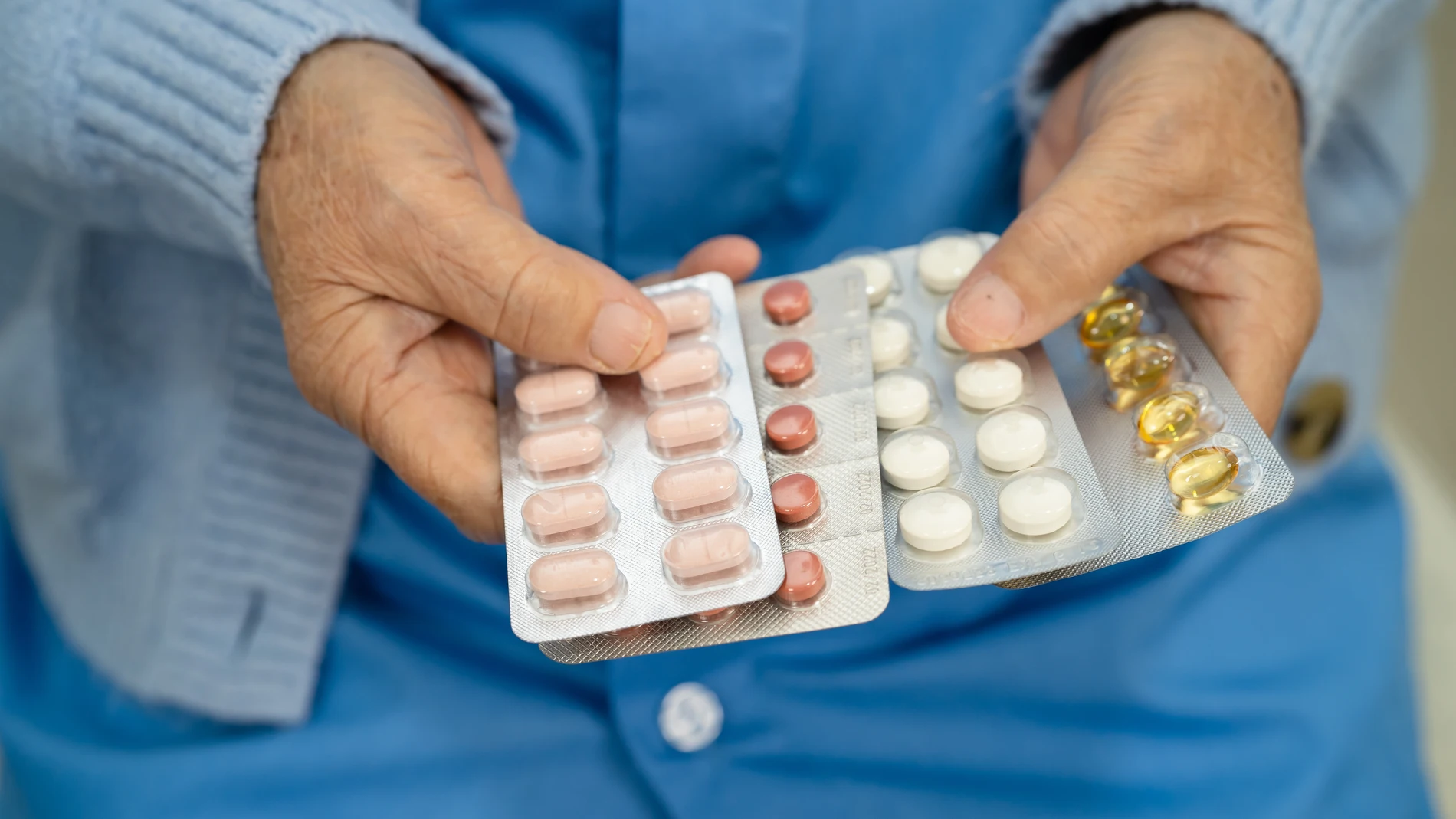 Paciente mayor sosteniendo cápsulas de antibióticos para el tratamiento de una infección en un hospital.