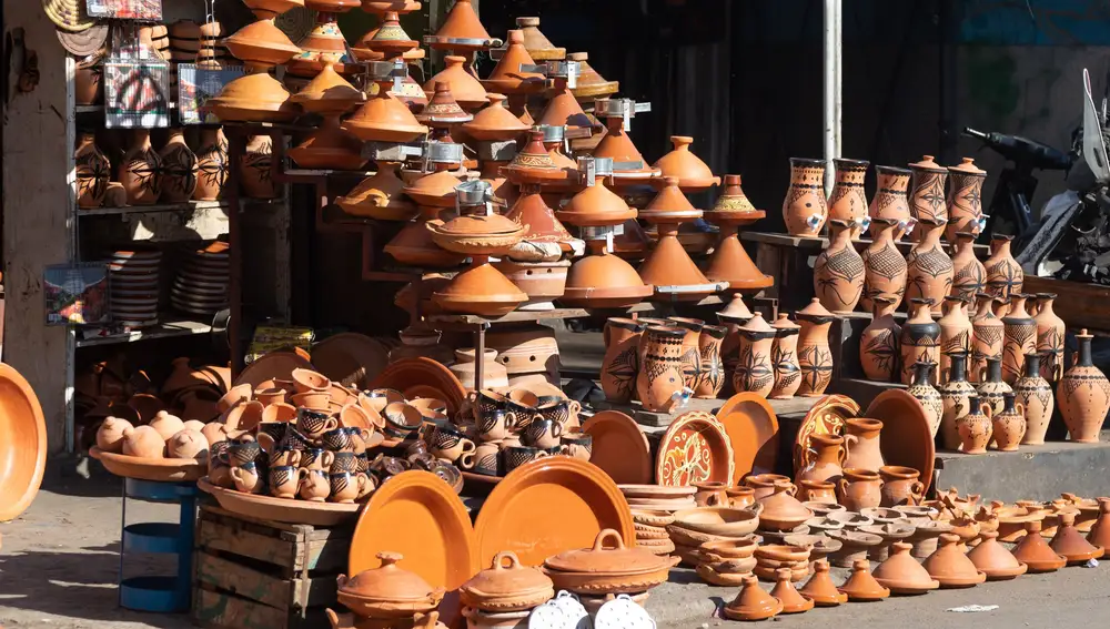 Puesto de venta de platos de cerámica y tagine en vestimentas tradicionales Casablanca Marruecos. Puesto de venta de cerámica tradicional plato de naranja marrón y tagine al estilo tberber Casablanca