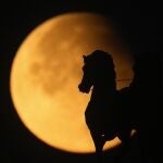 A supermoon rises behind a horse statue atop of Triumphal Arc during a partial lunar eclipse in Moscow, Russia, Wednesday, Sept. 18, 2024. 