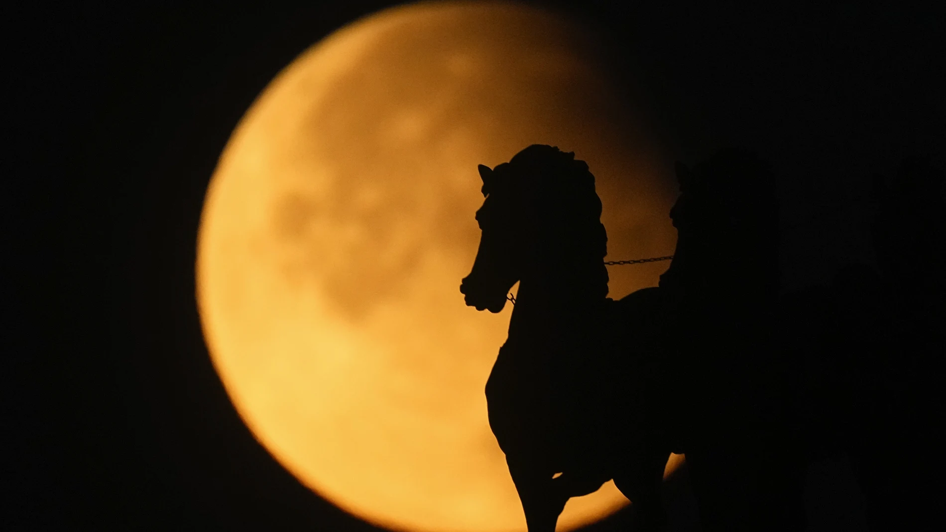 A supermoon rises behind a horse statue atop of Triumphal Arc during a partial lunar eclipse in Moscow, Russia, Wednesday, Sept. 18, 2024.