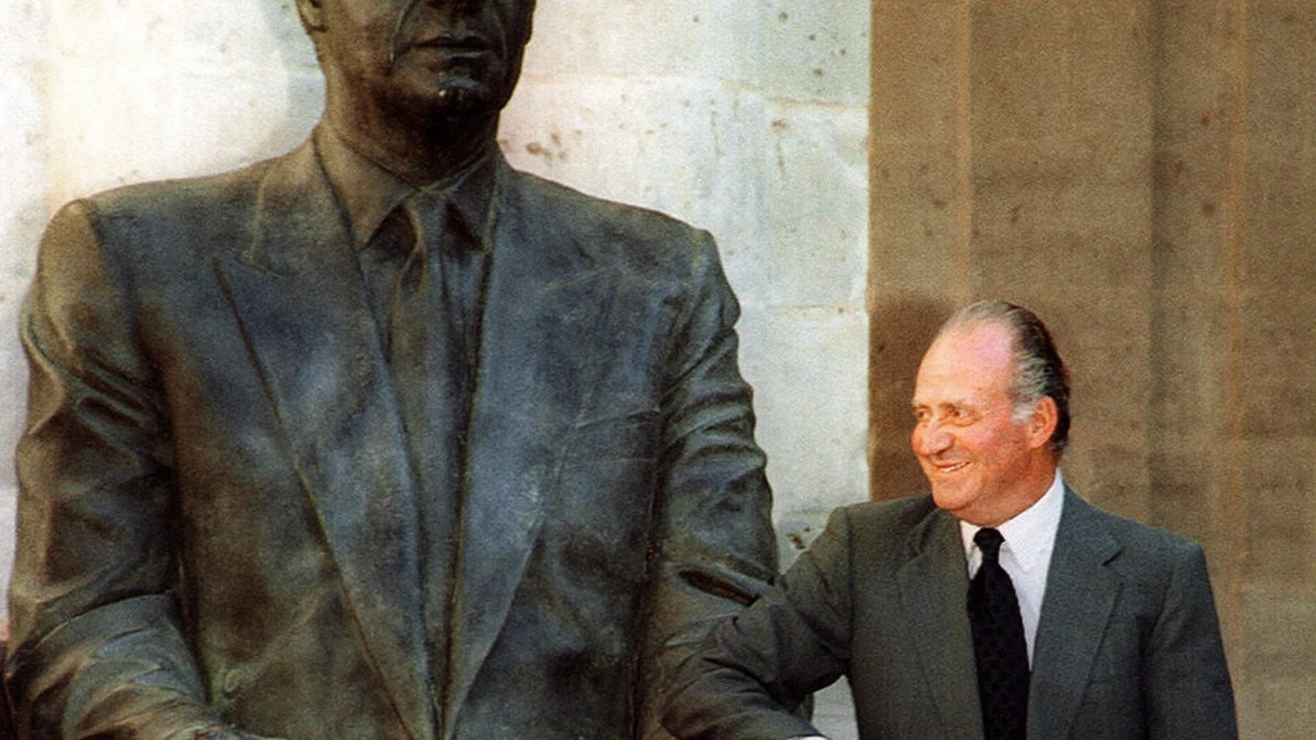 El rey Juan Carlos posa junto a la estatua que le reproduce y que descubrió hoy en el Patio Herrerano del antiguo Monasterio de San Benito el Real