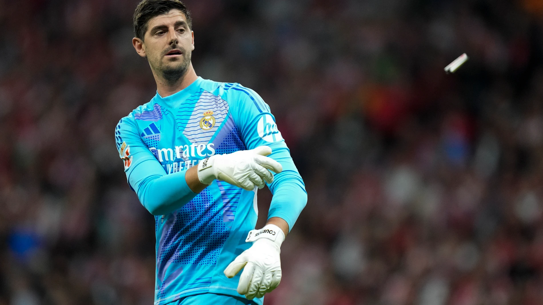 Real Madrid's goalkeeper Thibaut Courtois throws off the pitch a lighter, previously thrown by Atletico Madrid fans, during the La Liga soccer match between Atletico Madrid and Real Madrid at the Metropolitano stadium in Madrid, Spain, Sunday, Sept. 29, 2024. (AP Photo/Bernat Armangue)