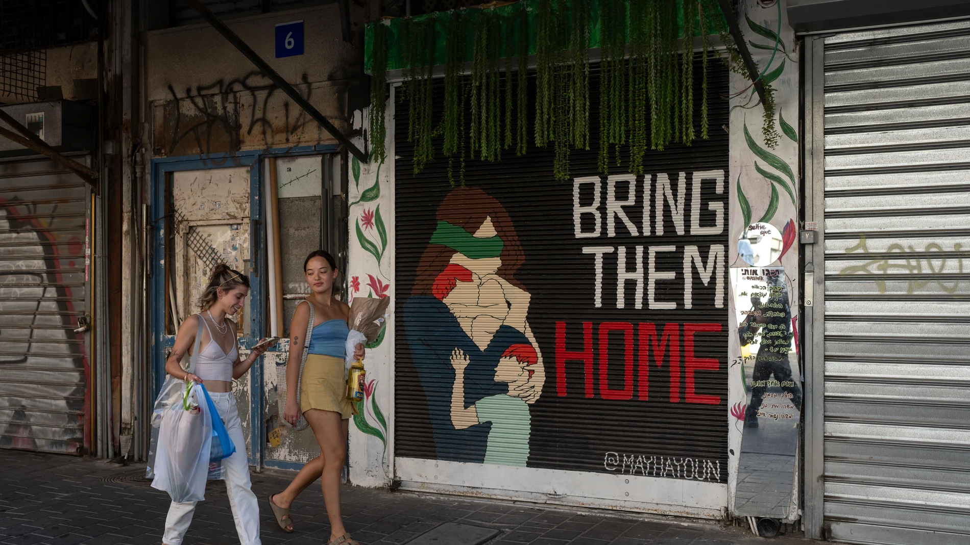 Women walk past graffiti calling for the release of hostages held by Hamas militants in the Gaza Strip for nearly a year, in the Carmel market Tel Aviv, Israel, Friday, Sept. 27, 2024. (AP Photo/Ohad Zwigenberg)