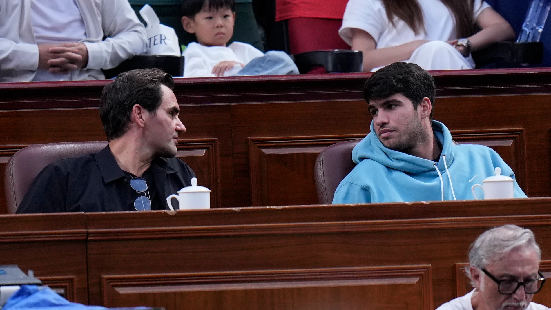 Tennis great Roger Federer, left talks to Carlos Alcaraz of Spain while they watch the men's singles finals match between Novak Djokovic of Serbia and Jannik Sinner of Italy for the Shanghai Masters tennis tournament at Qizhong Forest Sports City Tennis Center in Shanghai, China, Sunday, Oct. 13, 2024. (AP Photo/Andy Wong)