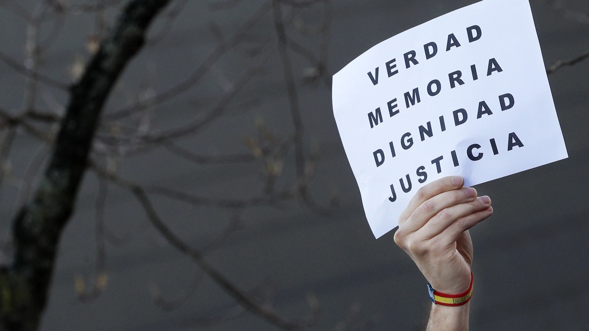 Una persona reivindica con un cartel "verdad, memoria, dignidad y justicia" frente al monumento a las víctimas del terrorismo levantado en la plaza del Baluarte de Pamplona