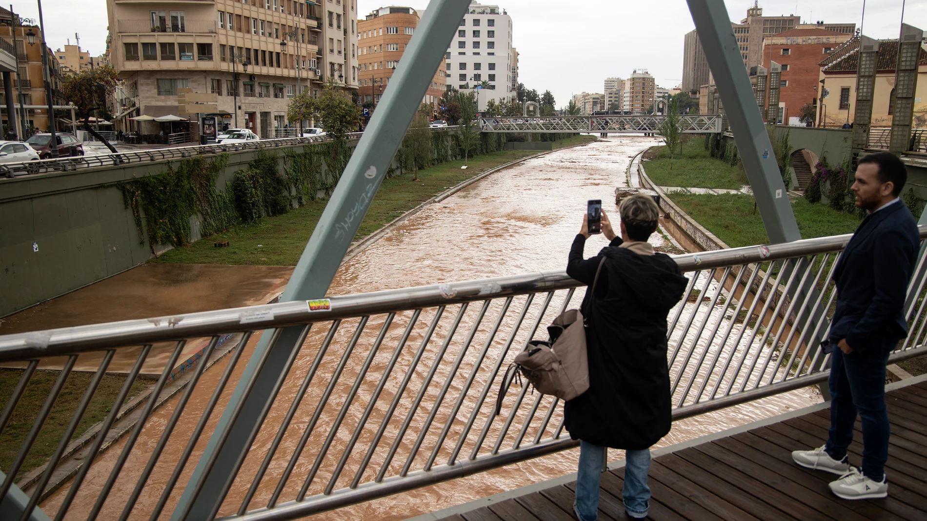 GRAFAND4210. MÁLAGA, 29/10/2024.- Varias personas fotografían el estado del río Guadalmedina a su paso por Málaga capital que se encuentra cubierto de agua por las fuertes lluvias caídas en las últimas horas debido al paso de la dana por Andalucía que está dejando innumerables incidencias.EFE/Daniel Pérez