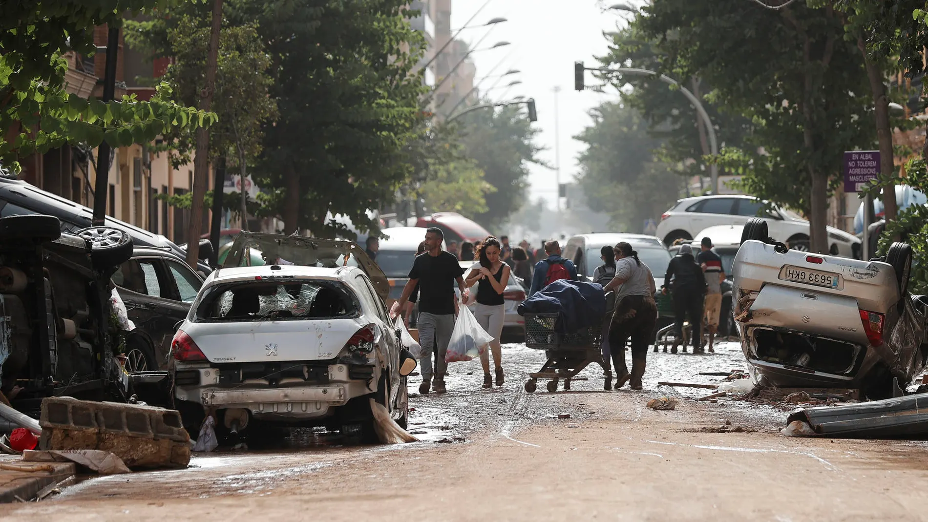 VALENCIA, 30/10/2024.- Unas personas caminan por una calle cubierta de lodo y llena de coches amontonados tras las intensas lluvias por la fuerte DANA hoy en Valencia