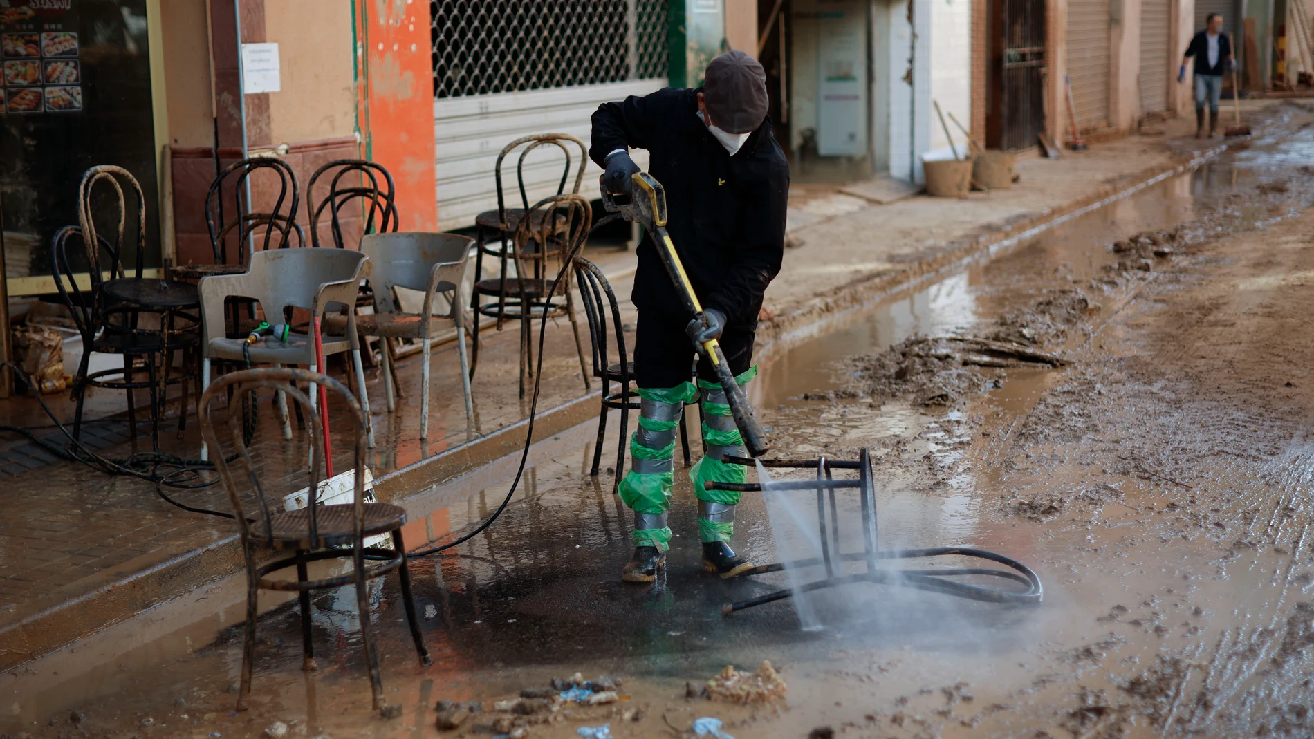 CATARROJA (VALENCIA), 12/11/2024.- Un voluntario limpia las sillas de un bar de Catarroja, este martes. La dana que dejó en Valencia más de dos centenares de muertos y decenas de desaparecidos, ha cambiado la vida de miles de personas y condicionado la economía, el transporte y la educación de la provincia; dos semanas después prosigue el goteo de mejoras en infraestructuras y servicios básicos y, en paralelo, la polémica política por la gestión de la catástrofe. EFE/Biel Aliño