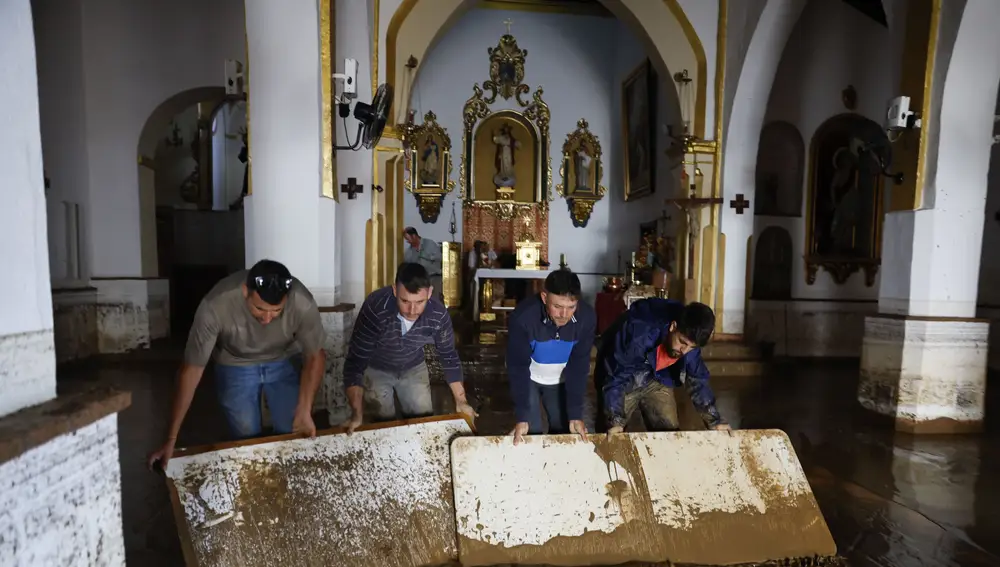 Vecinos colaboran con las labores de limpieza de la Iglesia de la Encarnación en la localidad malagueña de Benamargosa este jueves. La dana sobre el sur y extremo oriental del país, con cuantiosos daños en las últimas horas, rescates y vías cortadas por inundaciones, como en Málaga -ya sin riesgo- empieza a remitir pero el temporal azotará aún hoy a Andalucía, que está en alerta naranja (riesgo importante), así como a Valencia, aunque solo hasta media mañana.