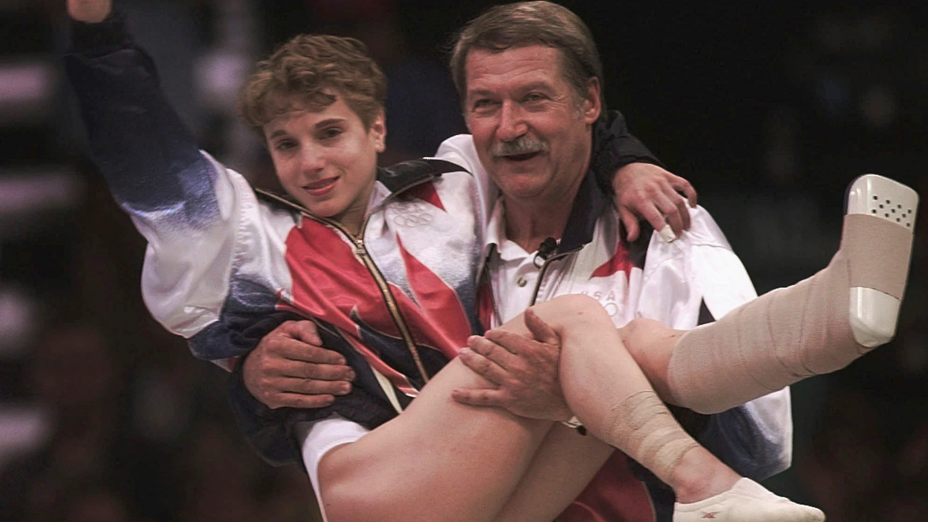 FILE - USA's Kerri Strug is carried by her coach, Bela Karolyi, as she waves to the crowd on her way to receiving her gold medal for the women's team gymnastics competition, at the Centennial Summer Olympic Games in Atlanta, July 23, 1996. Strug had two torn ligaments and a sprained ankle from the vault competition. (AP Photo/Susan Ragan, File)