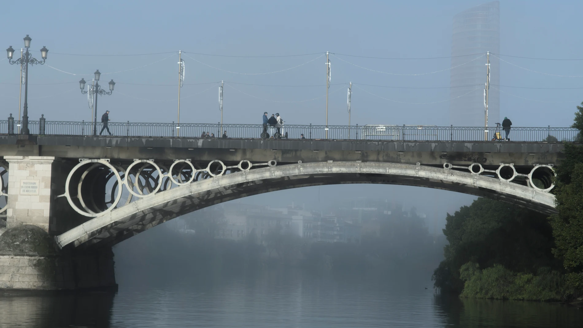 GRAFAND5805. SEVILLA, 09/01/2025.- Varias personas caminan por el Puente de Triana en Sevilla que ha amanecido con niebla este jueves que en Andalucía las temperaturas mínimas irán en ascenso. EFE/ Raúl Caro.