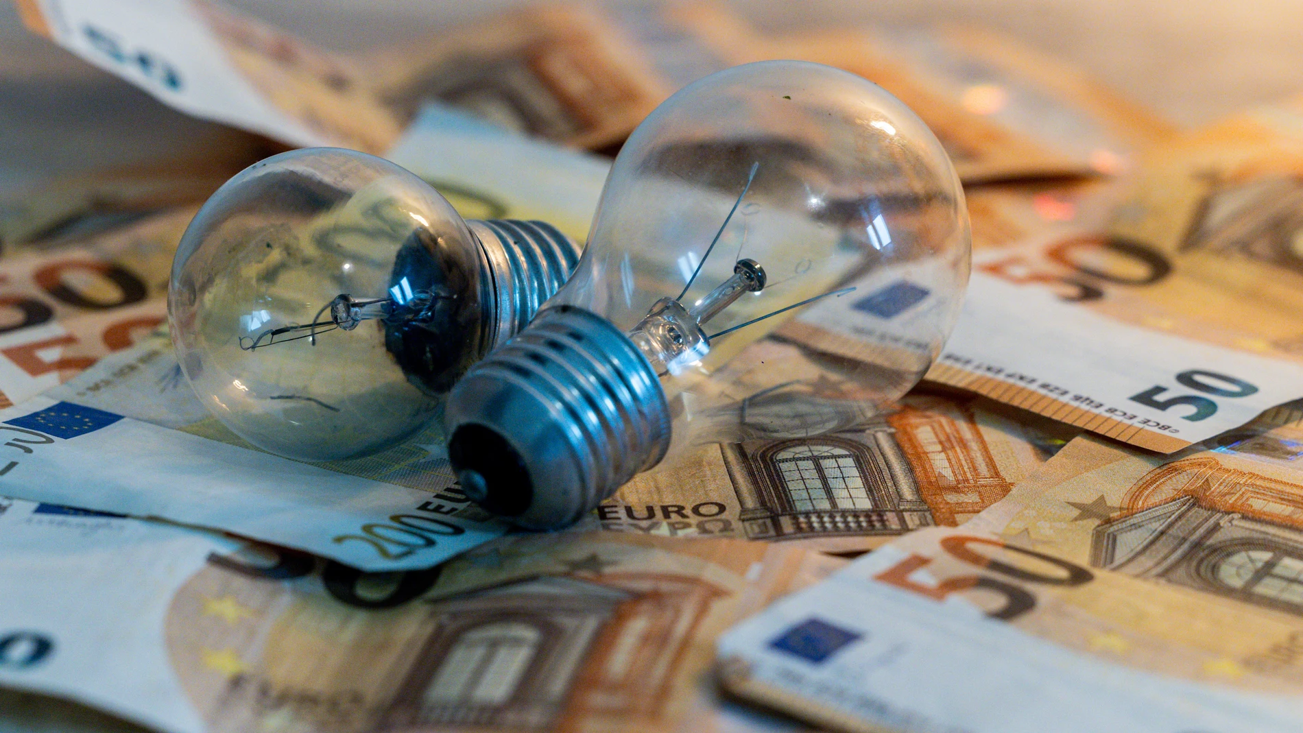 Dos bombillas sobre billetes, a 9 de enero de 2025, en Madrid (España). El Gobierno central ha eliminado de manera definitiva las reducciones temporales que, desde junio de 2021, venía aplicando para paliar la inflación de precios en materia energética, derivada de la Guerra de Ucrania. Esto se traduce en un incremento del IVA de la electricidad del 10 al 21 por ciento, que desde este mes de enero se reflejará en la factura de la luz. Los expertos estiman que, en función del consumo de cada h...