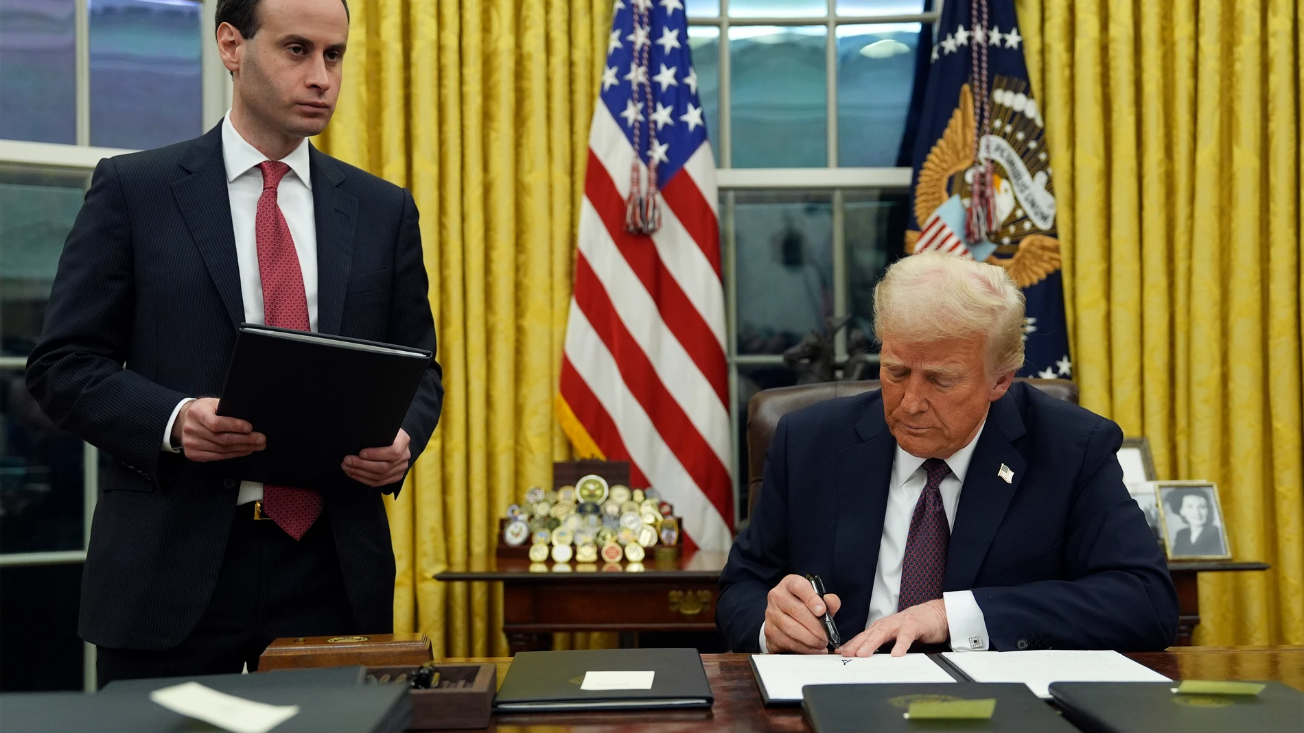 President Donald Trump signs an executive order to create the Department of Government Efficiency (DOGE) in the Oval Office of the White House, Monday, Jan. 20, 2025, in Washington, as White House staff secretary Will Scharf watches. (AP Photo/Evan Vucci)