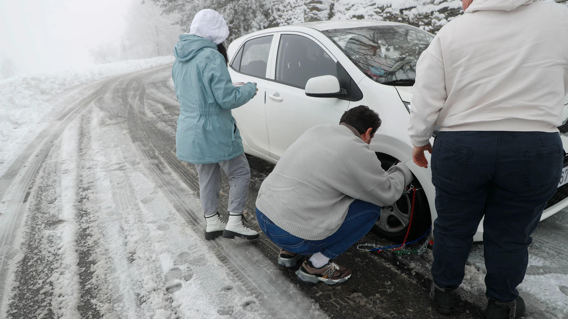 Varias personas colocan las cadenas para circular por una carretera cubierta de nieve, este jueves en Pedrafita do Cebreiro. A pesar de que el anticiclón irá ganando terreno los próximos días, este jueves la borrasca Ivo aún deja un importante temporal marítimo, con olas de casi 10 metros en las costas del norte peninsular, rachas huracanadas de viento por encima de los 130 km/h y copiosas nevadas en montañas de la mitad norte del país. EFE/ Eliseo T...