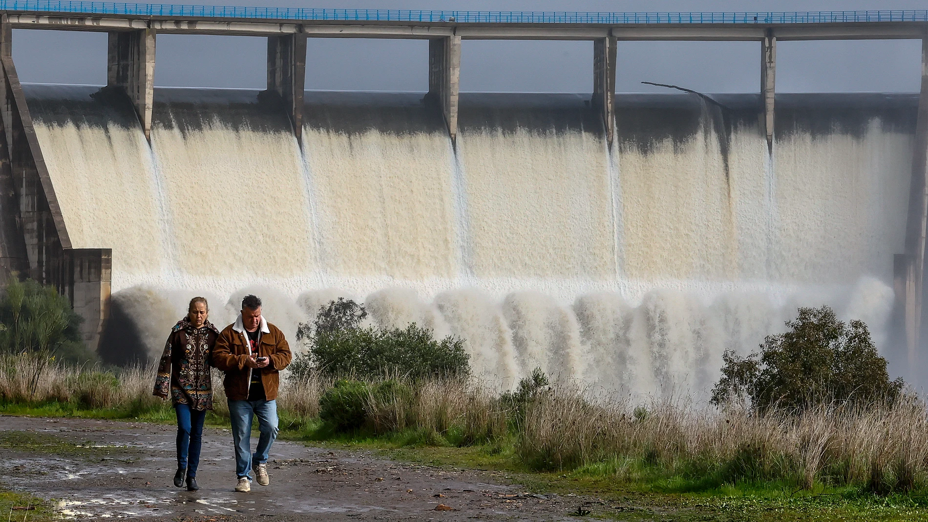 SEVILLA, 10/03/2025.- Dos personas pasean junto al embalse de El Gergal en Guillena ( Sevilla) que desembalsa agua tras alcanzar el limite de su capacidad. La última borrasca ha dejado abundante agua en los embalses que abastecen a Andalucía, aunque hay grandes contrastes entre la zona oriental, con el embalse almeriense de Cuevas de Almanzora, al 9,3 % de su capacidad de almacenamiento, y la parte occidental, con el de Melonares (Sevilla), al 104 %.EFE /José Manuel Vidal