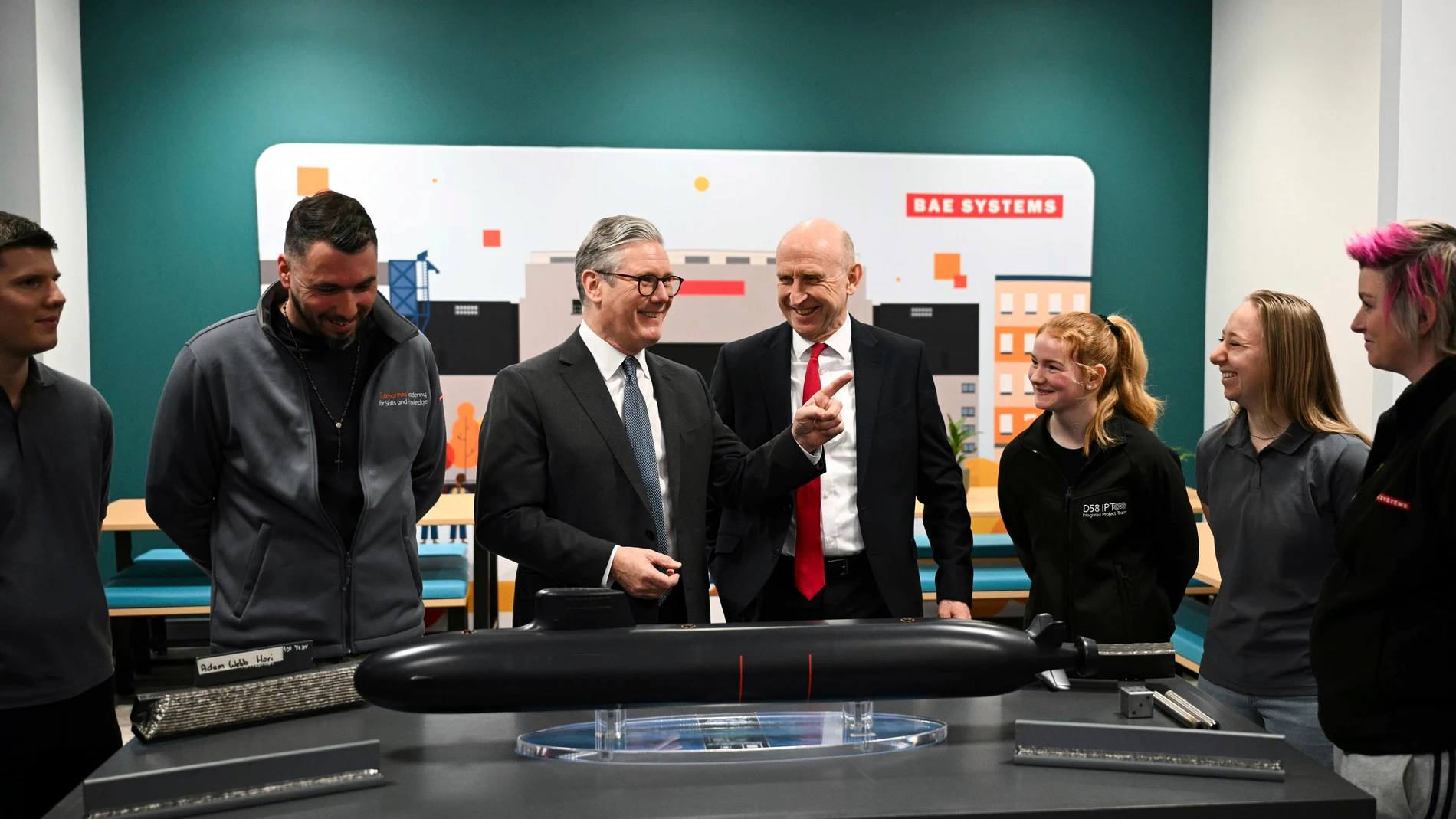 Britain's Prime Minister Keir Starmer, center left, and Defence Secretary John Healey, center right, meet with BAE system apprentices as they look at a submarine model during a joint visit in Barrow-in-Furness, England, Thursday March 20, 2025. (Oli Scarff/Pool via AP)