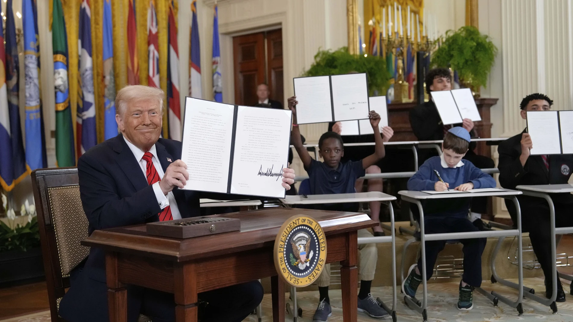 President Donald Trump, left, holds up a signed executive order as young people hold up copies of the executive order they signed at an education event in the East Room of the White House in Washington, Thursday, March 20, 2025.