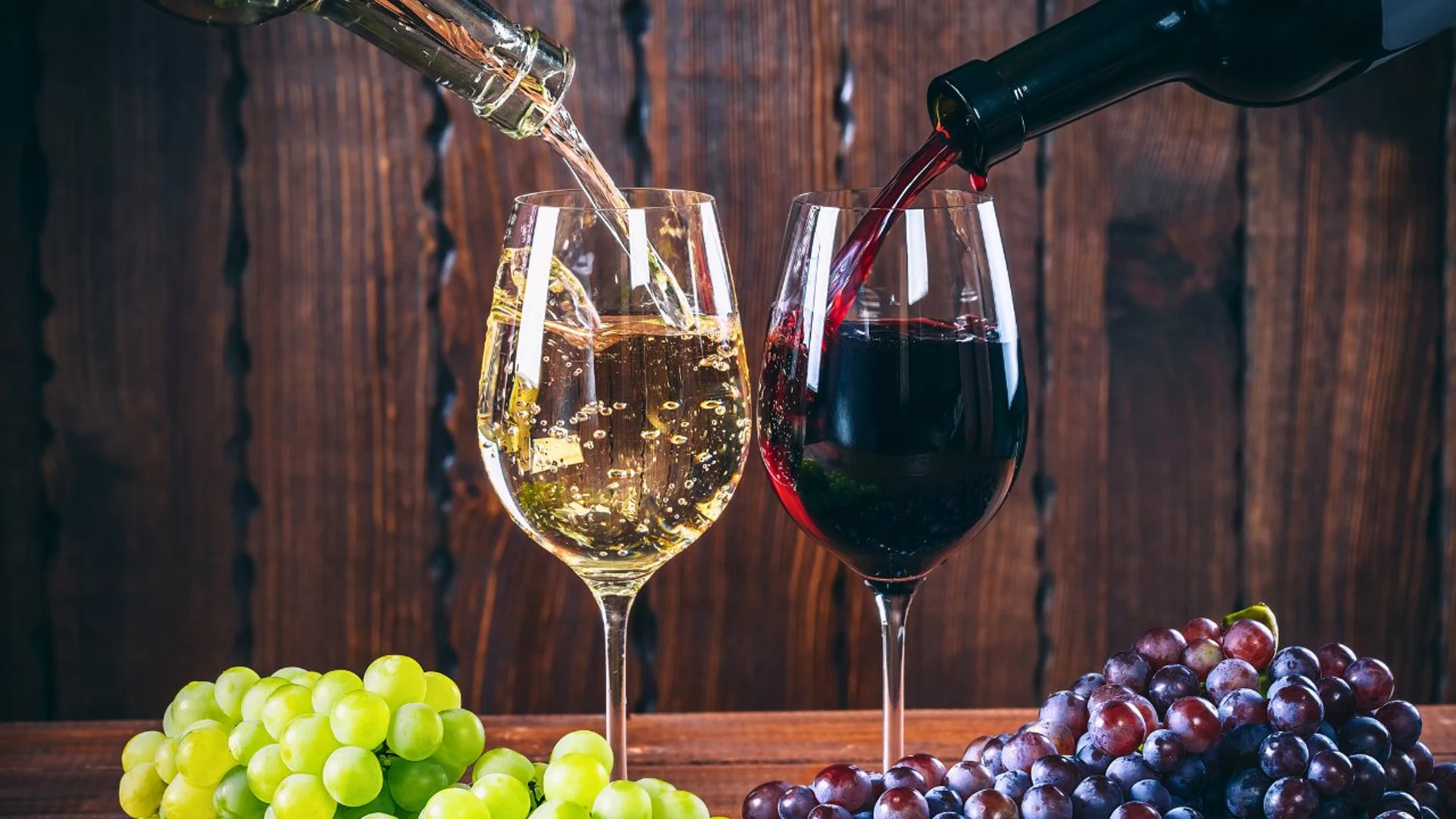 Una copa de vino blanco y una copa de vino tinto sobre uvas