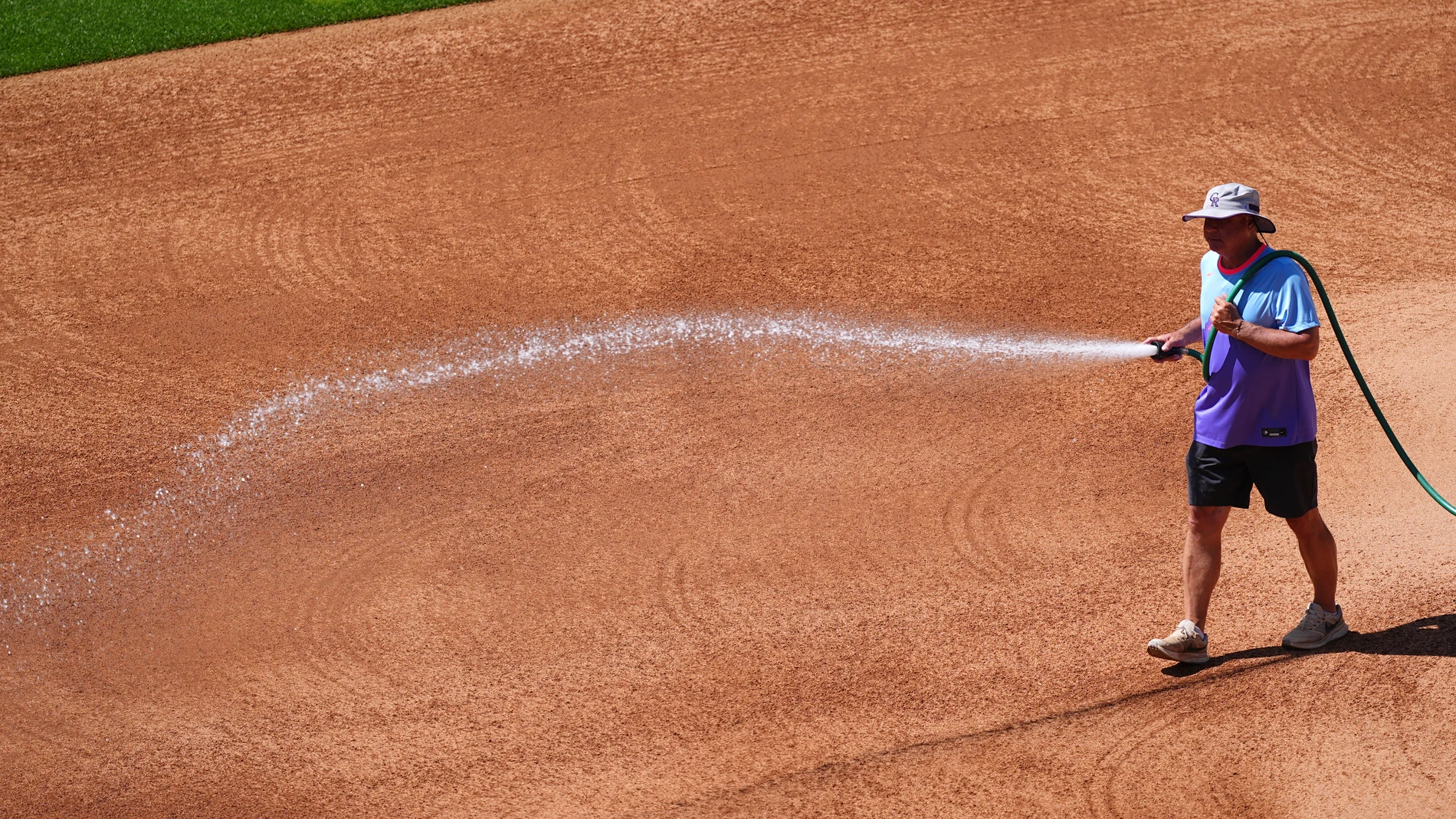 Coors Field head groundskeeper Mark Razum wets down the skin of the infield for a baseball game between the Arizona Diamondbacks and the Colorado Rockies as a heat dome packing triple-digit daytime high temperatures sweeps over the intermountain west Friday, June 20, 2025, in Denver. (AP Photo/David Zalubowski)
