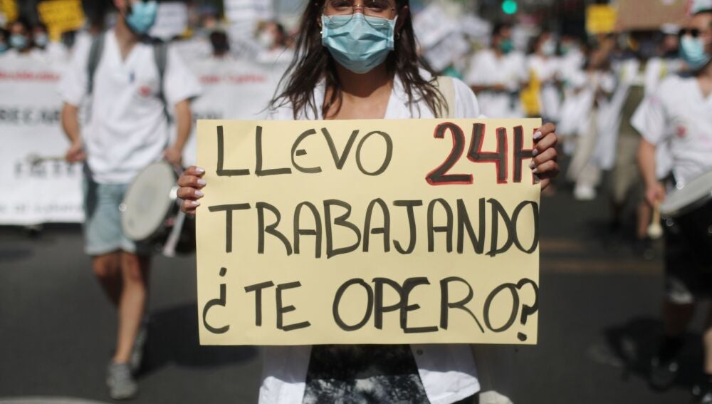 Una mujer sujeta una pancarta en la que se lee 'Llevo 24h trabajando, &iquest;te opero?' durante una manifestaci&oacute;n de los m&eacute;dicos internos residentes (MIR) en Madrid 