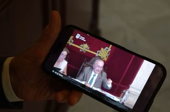 El alcalde de Málaga sujeta un teléfono móvil en el que reproduce el vídeo viral del pleno de julio