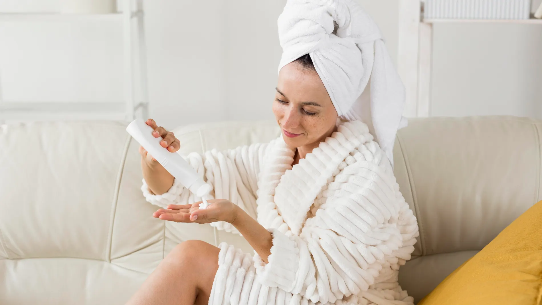 Mujer en albornoz aplicando crema corporal después de la ducha como parte de su rutina after sun
