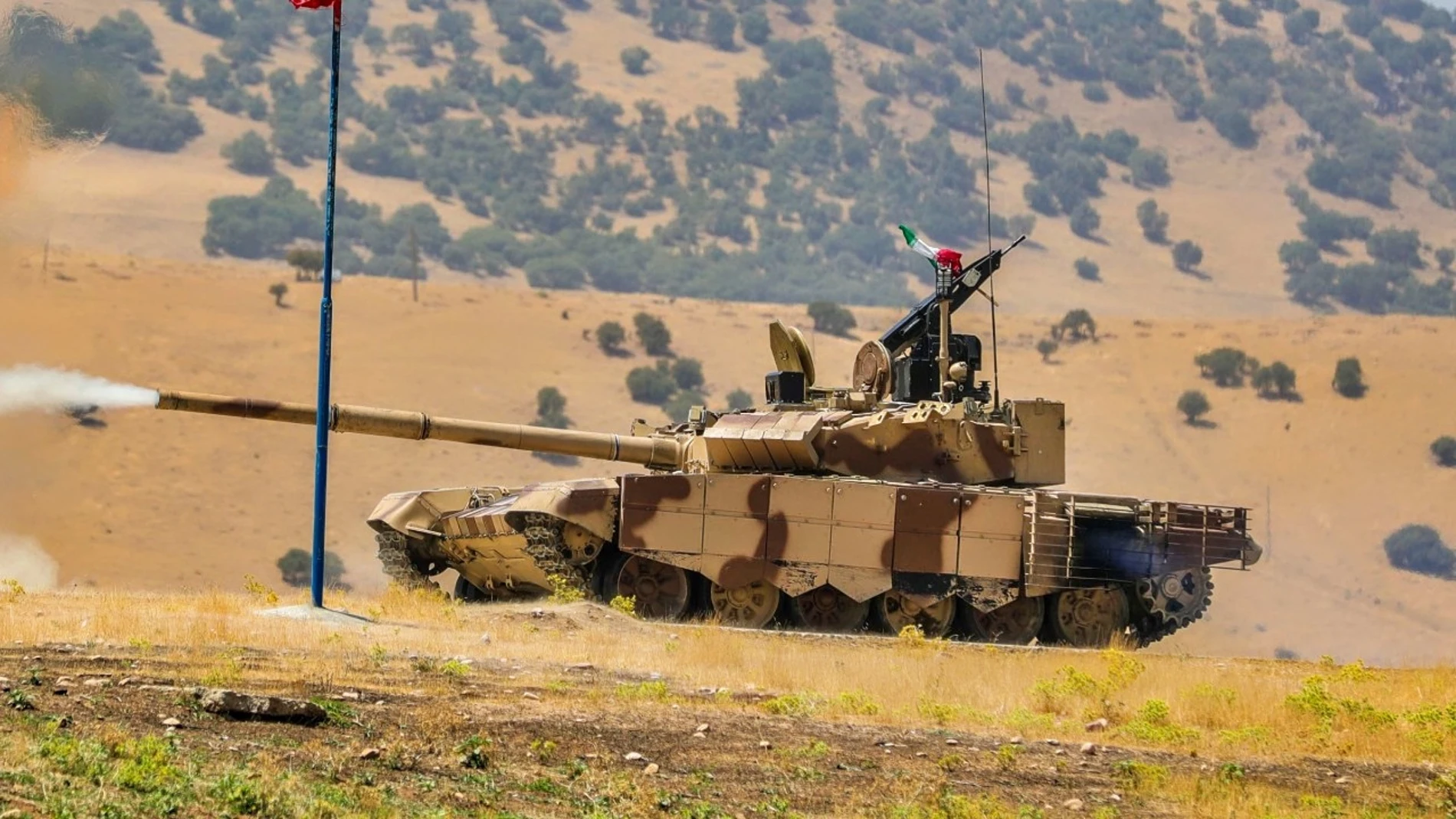 Aparece un carro de combate de color camuflaje marrón y tierra disparando durante unas maniobras
