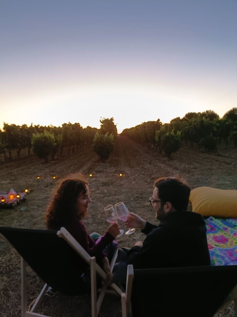 Una pareja disfruta de una puesta de sol mientras brinda con un vino en un viñedo durante una cata de estrellas organizada por Bodega La Olmilla