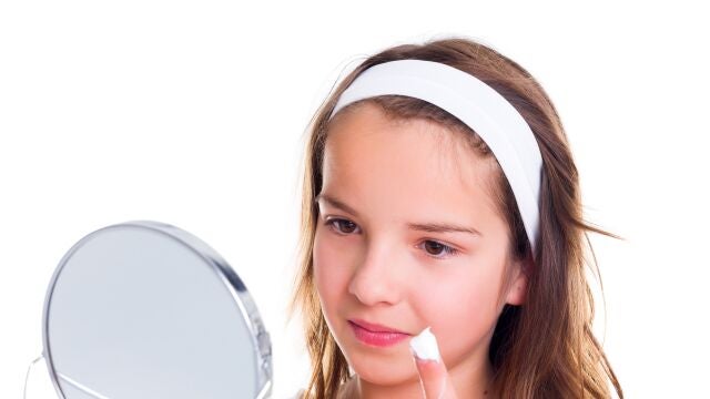 Adolescente mirándose al espejo y untándose la cara con crema. 