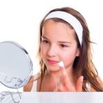 Adolescente mirándose al espejo y untándose la cara con crema. 