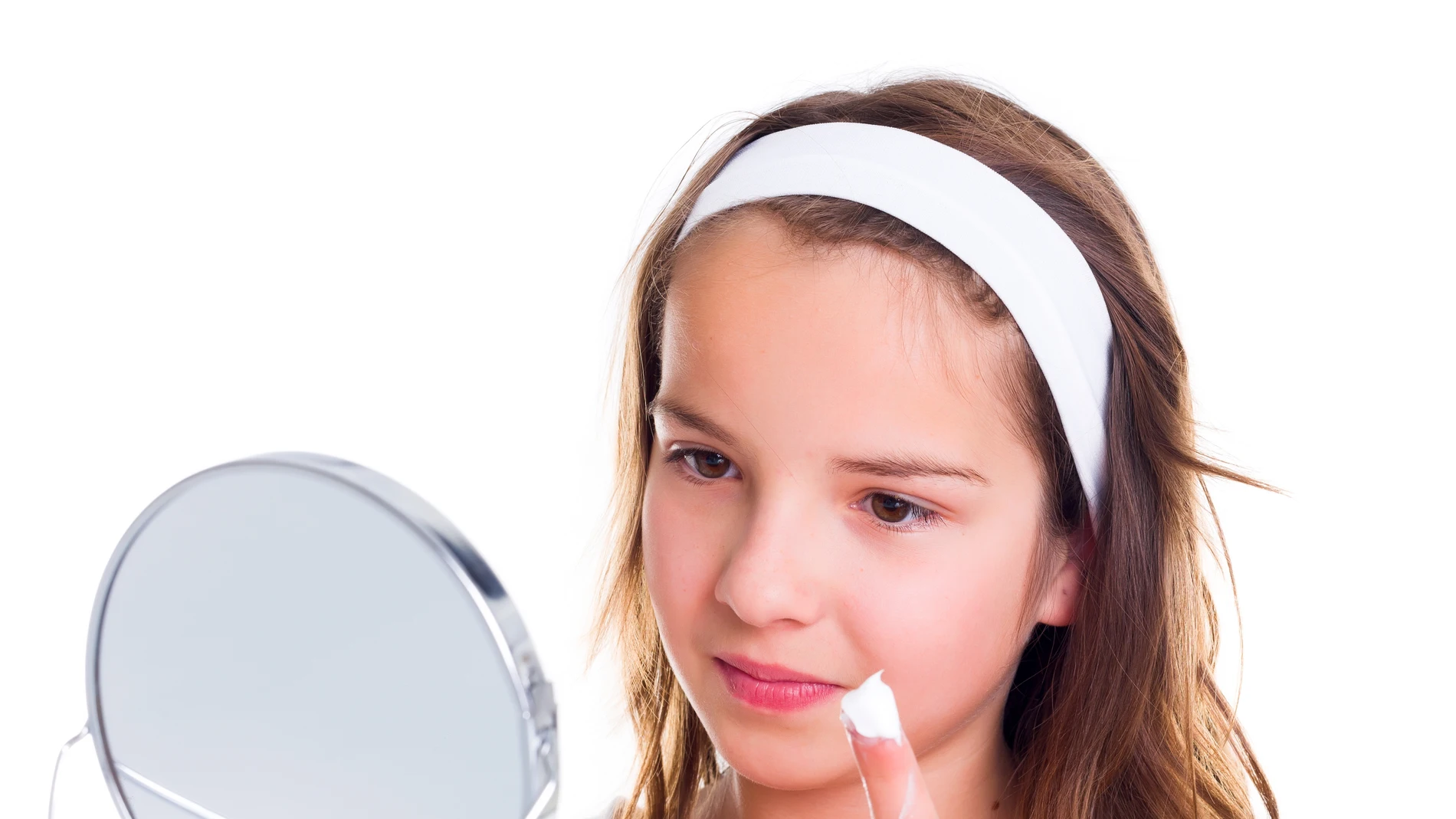 Adolescente mirándose al espejo y untándose la cara con crema.