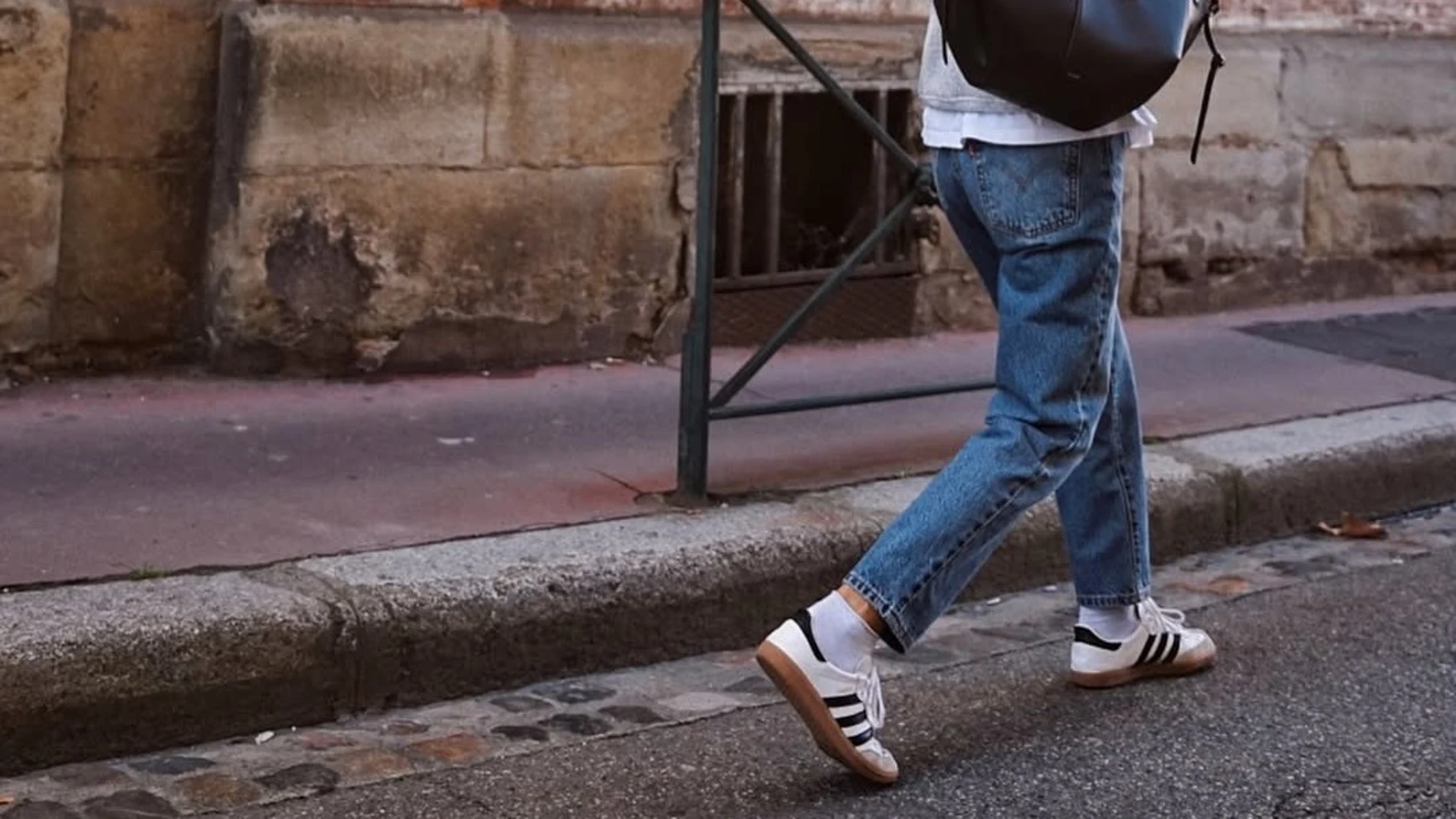 Influencer con deportivas blancas con franjas negras y suela marrón, en un conjunto casual con vaqueros.