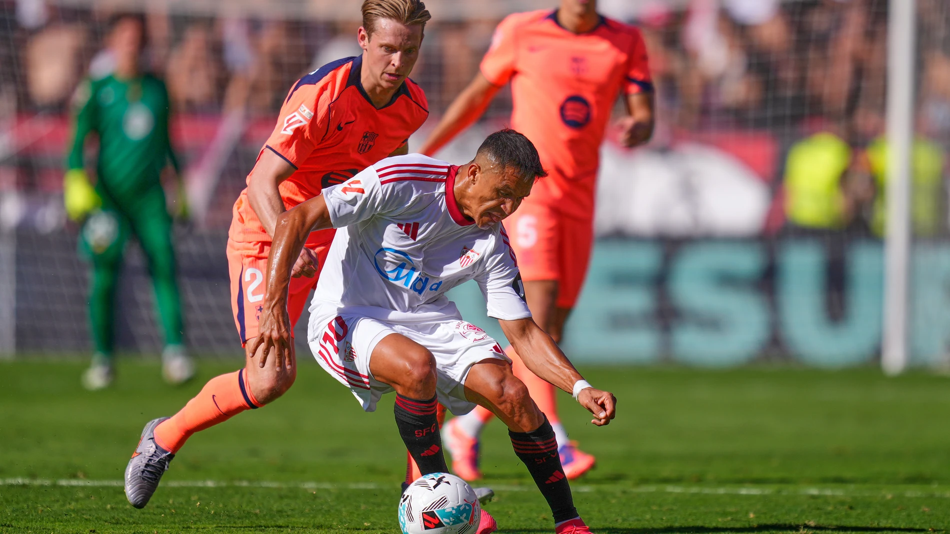 Sevilla's Alexis Sanchez, centre, challenges for the ball with Barcelona's Frenkie de Jong during the Spanish La Liga soccer match between Sevilla and Barcelona at the Ramon Sanchez Pizjuan stadium in Seville, Spain, Sunday, Oct. 5, 2025. (AP Photo/Jose Breton)