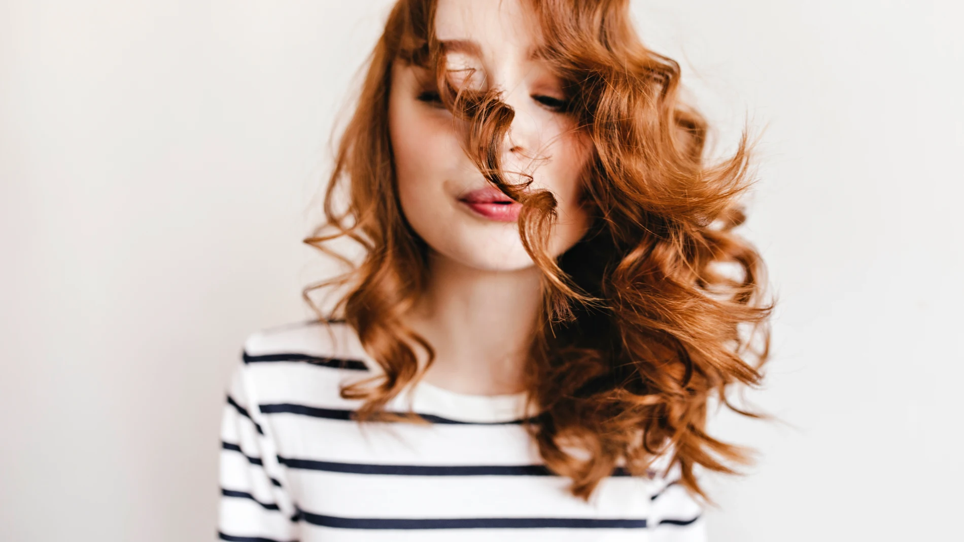 Mujer pelirroja con el pelo rizado y brillante, símbolo de hidratación y cuidado capilar.