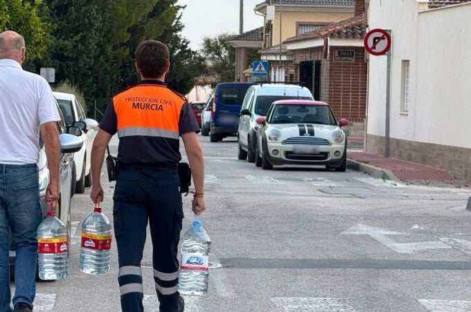 Un miembro de Protección Civil ayuda a un vecino a transportar agua