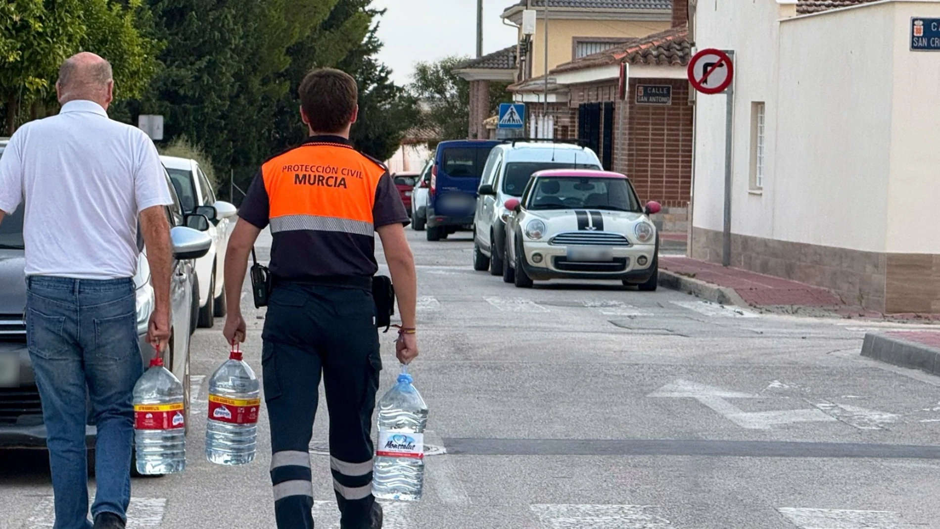 Un miembro de Protección Civil ayuda a un vecino a transportar agua