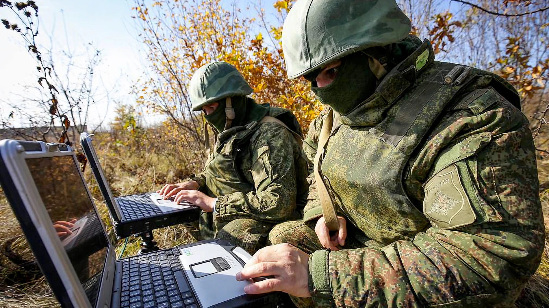 Soldados con uniforme de camuflaje manejando dos ordenadores portátiles en mitad de un ataque
