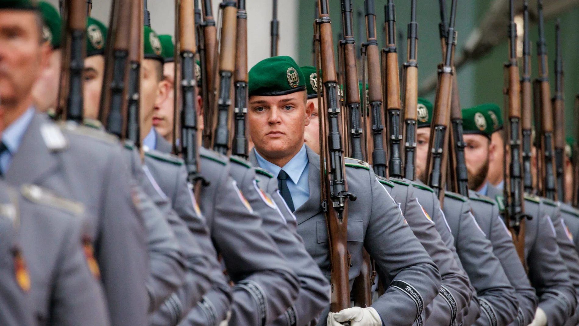 Soldados con uniforme gris y boinas verdes sosteniendo fusiles de cerrojo mientras marchan en formación