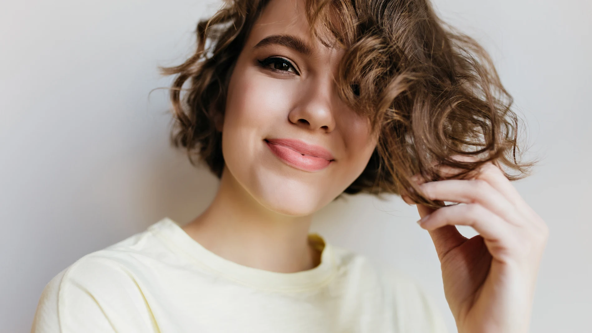 Retrato de una mujer joven con media melena rizada tocando su cabello, símbolo de un pelo sano y con volumen.