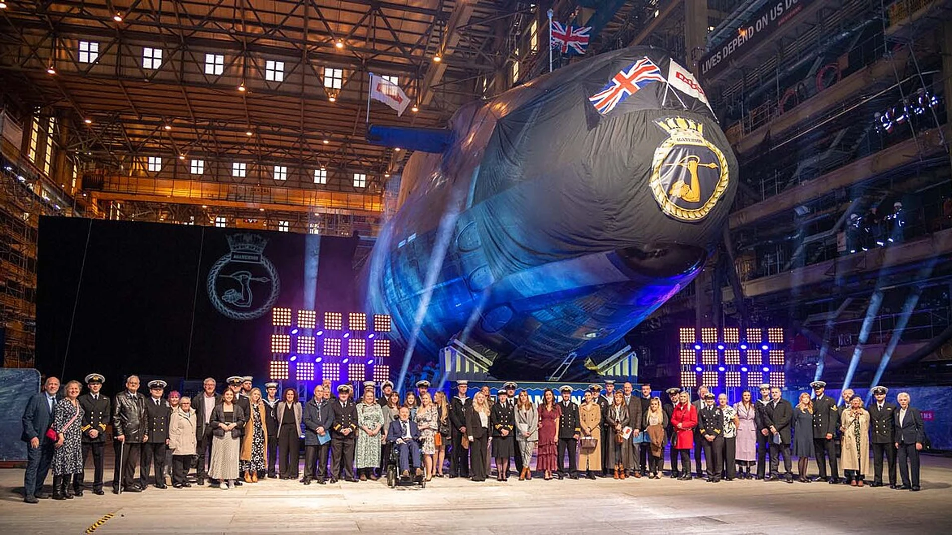 Una fila de autoridades con uniformes militares y de gala delante de un submarino en el dique seco