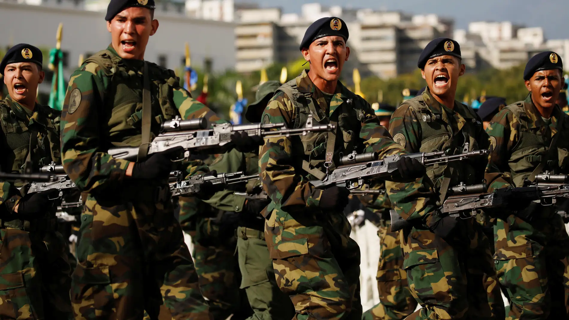 Soldados con uniforme de camuflaje y boina negra desfilando con sus fusiles de asalto AK al frente