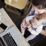 Mujer trabajando en su portátil con su hija en el regazo